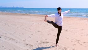 Woman makes yoga on sea beach raises her leg and holds it hand in balance pose. stock video Woman makes yoga on sea beach raises her leg and holds it hand in balance pose. stock video