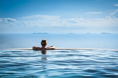 Woman relaxing in infinity swimming pool looking at view