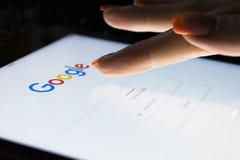 A woman`s hand is touching screen on tablet computer iPad Pro at night for searching on Google search engine. Google is the most