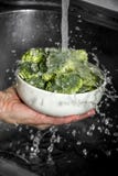 Woman`s hand washing broccoli under running water at the kitchen sink. Royalty Free Stock Image Woman`s hand washing broccoli under running water at the kitchen sink. Royalty Free Stock Image
