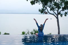 Woman sits, raising her hands, on the edge of the pool. stock photo Woman sits, raising her hands, on the edge of the pool. stock photo