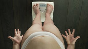 Woman standing on scales with word obese on screen, failed dieting, annoyed