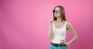 Woman in sunglasses licking lollipop over pink background