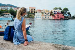 Woman tourist wearing blue dress sitting on the pier and looking to the picturesque bay. Assos village with beautiful royalty free stock images Woman tourist wearing blue dress sitting on the pier and looking to the picturesque bay. Assos village with beautiful royalty free stock images