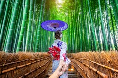 Woman wearing japanese traditional kimono holding man`s hand and leading him to Bamboo Forest in Kyoto, Japan