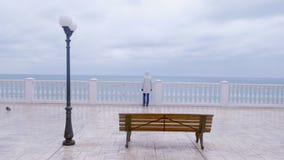 Woman in white jacket and hood on beautiful terrace with sea view on waterfront. Back view. stock footage Woman in white jacket and hood on beautiful terrace with sea view on waterfront. Back view. stock footage