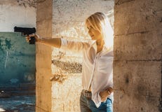Woman in a white shirt shoots a pistol in an abandoned building from around the corner