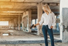 Woman in white shirt stands in an abandoned building, shoots a gun