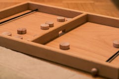 Wooden bard game where you shoot round wooden blocks through opening with help of an elastic band. Two players visible
