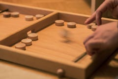 Wooden bard game where you shoot round wooden blocks through opening with help of an elastic band. Two players visible