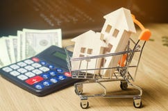 Wooden houses in a supermarket trolley, money and a calculator. Real Estate Market Analytics. Real estate concept. Sale and