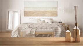 Wooden table top or shelf with aromatic sticks bottles over blurred modern bedroom with classic bed, white architecture interior d