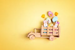 Wooden toy truck with Easter homemade gingerbread cookies  in the back on yellow background. Funny Easter decoration