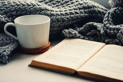 Woolen scarf, a cup of tea and book on the windowsill. Hygge and cozy autumn concept