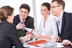 Working in a group. Group of four young businesspeople discussing different questions gathered together around the table with the laptop, drinks and documents on Working in a group. Group of four young businesspeople discussing different questions gathered together around the table with the laptop, drinks and documents on