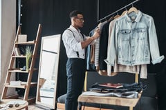 Working On New Order. Thoughtful Young Man Choosing Clothes From Stock Image Working On New Order. Thoughtful Young Man Choosing Clothes From Stock Image
