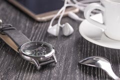 Wristwatch i telefon komórkowy z hełmofonami i filiżanka kawy na ciemnym drewnianym stole zdjęcia stock Wristwatch i telefon komórkowy z hełmofonami i filiżanka kawy na ciemnym drewnianym stole zdjęcia stock