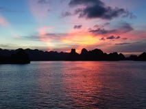 Wschód słońca w Halong zatoce Z pomarańczowych i błękita brzmieniami Z niektóre statkami przy tłem obrazy royalty free Wschód słońca w Halong zatoce Z pomarańczowych i błękita brzmieniami Z niektóre statkami przy tłem obrazy royalty free