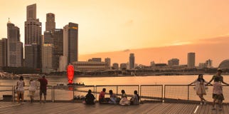 Wärmen Sie bunten Sonnenuntergang auf modernen Gebäuden und Architektur in Marina Bay Sands mit den Leuten, die auf Docks und auf lizenzfreies stockfoto Wärmen Sie bunten Sonnenuntergang auf modernen Gebäuden und Architektur in Marina Bay Sands mit den Leuten, die auf Docks und auf lizenzfreies stockfoto