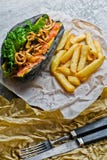 Würstchen mit Rindfleischwurst und karamellisierten Zwiebeln in einem schwarzen Brötchen Grauhintergrund, Seitenansicht lizenzfreie stockfotos Würstchen mit Rindfleischwurst und karamellisierten Zwiebeln in einem schwarzen Brötchen Grauhintergrund, Seitenansicht lizenzfreie stockfotos