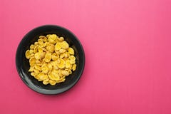 Yellow corn flakes in a black plate on a pink background. Place for the text royalty free stock images Yellow corn flakes in a black plate on a pink background. Place for the text royalty free stock images