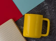 Yellow mug with notebook on dark stone background. Blue and red paper. With copy space royalty free stock image Yellow mug with notebook on dark stone background. Blue and red paper. With copy space royalty free stock image