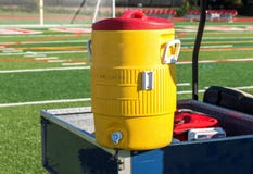 Yellow water cooler on a blue cart with soccer net in background stock images Yellow water cooler on a blue cart with soccer net in background stock images