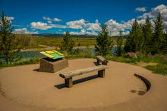 YELLOWSTONE, MONTANA, USA MAY 24, 2018: Beautiful outdoor view of informative sign and wooden public chair with a view stock images YELLOWSTONE, MONTANA, USA MAY 24, 2018: Beautiful outdoor view of informative sign and wooden public chair with a view stock images