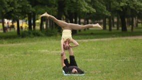 Yoga di pratica di acro delle belle coppie I giovani istruttori di yoga praticano in un parco della città su erba verde Due riusc video d archivio Yoga di pratica di acro delle belle coppie I giovani istruttori di yoga praticano in un parco della città su erba verde Due riusc video d archivio