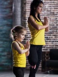 Yoga practicante de la ropa de los deportes de la madre que lleva y de la hija junta que medita la colocación en una pierna con l fotos de archivo Yoga practicante de la ropa de los deportes de la madre que lleva y de la hija junta que medita la colocación en una pierna con l fotos de archivo