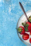 Yogur orgánico en un cuenco con las fresas recientemente cortadas en un azul Foto de archivo libre de regalías Yogur orgánico en un cuenco con las fresas recientemente cortadas en un azul Foto de archivo libre de regalías