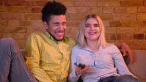 Young african guy strangles his blonde caucasian girlfriend watching TV in cozy home atmosphere. stock video footage Young african guy strangles his blonde caucasian girlfriend watching TV in cozy home atmosphere. stock video footage