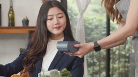 Young Asian business women pay contactless at coffee shop. Asian happy girl barista waiter wear gray apron holding credit card
