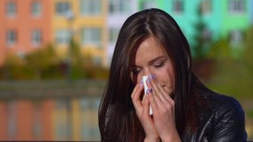 Young attractive girl, caught a cold on the street, wipes her nose with a napkin.