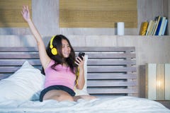Young attractive and happy Asian Chinese woman with yellow headphones listening to music in mobile phone on bed at home smiling ha stock image Young attractive and happy Asian Chinese woman with yellow headphones listening to music in mobile phone on bed at home smiling ha stock image