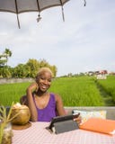 Young attractive and happy black african American woman working online with digital tablet pad drinking coconut sitting at outdoor Stock Photography Young attractive and happy black african American woman working online with digital tablet pad drinking coconut sitting at outdoor Stock Photography