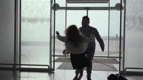 Young bearded caucasian man entering the glass airport door with luggage. Little cheerful girl running up to her father