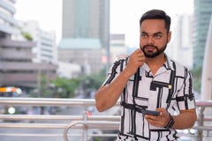 Young bearded Indian man thinking and using phone against view of the city streets royalty free stock images Young bearded Indian man thinking and using phone against view of the city streets royalty free stock images