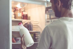 Young bearded man opens the bottle of milk standing near fridge at home stock images Young bearded man opens the bottle of milk standing near fridge at home stock images