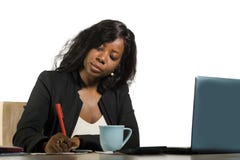 Young Beautiful And Busy Black Afro American Businesswoman Writing Notes On Desk Working With Laptop Computer At Company Office In Stock Photos