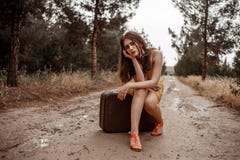Young beautiful girl in a yellow vintage dress posing on a muddy country road, sitting on a retro suitcase stock images Young beautiful girl in a yellow vintage dress posing on a muddy country road, sitting on a retro suitcase stock images
