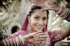 Young beautiful Indian Hindu bride standing under tree with painted hands raised