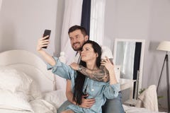 Young beautiful and loving couple take selfie picture on smartphone camera while sitting in bed at the morning royalty free stock image Young beautiful and loving couple take selfie picture on smartphone camera while sitting in bed at the morning royalty free stock image
