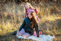 Young beautiful mother with her daughter on a walk on a sunny autumn day. Daughter is trying to put her hat on mother, they are la stock photo Young beautiful mother with her daughter on a walk on a sunny autumn day. Daughter is trying to put her hat on mother, they are la stock photo