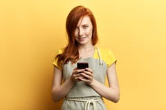 Young beautiful red-haired gardener with apron sending a message with the mobile stock photos Young beautiful red-haired gardener with apron sending a message with the mobile stock photos