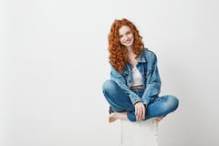 Young beautiful redhead girl smiling looking at camera sitting on box over white background. Copy space. stock photos Young beautiful redhead girl smiling looking at camera sitting on box over white background. Copy space. stock photos