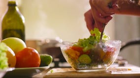 Young beautiful woman in home clothes is cooking in the kitchen. She makes some fresh salad with green lettuce. Cucumbers and also red tomatoes. The girl is Young beautiful woman in home clothes is cooking in the kitchen. She makes some fresh salad with green lettuce. Cucumbers and also red tomatoes. The girl is