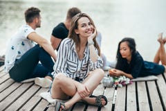 Young beautiful woman relaxing by river in company of friends stock photo Young beautiful woman relaxing by river in company of friends stock photo