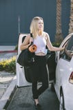 Young Blond Female Millennial Exits Her Car with Gym Bag and Yoga Mat to Exercise Smiling with Happy Expression stock image Young Blond Female Millennial Exits Her Car with Gym Bag and Yoga Mat to Exercise Smiling with Happy Expression stock image