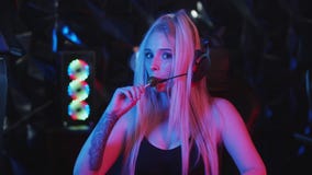 Young blonde woman gamer in big headphones licking a lollipop